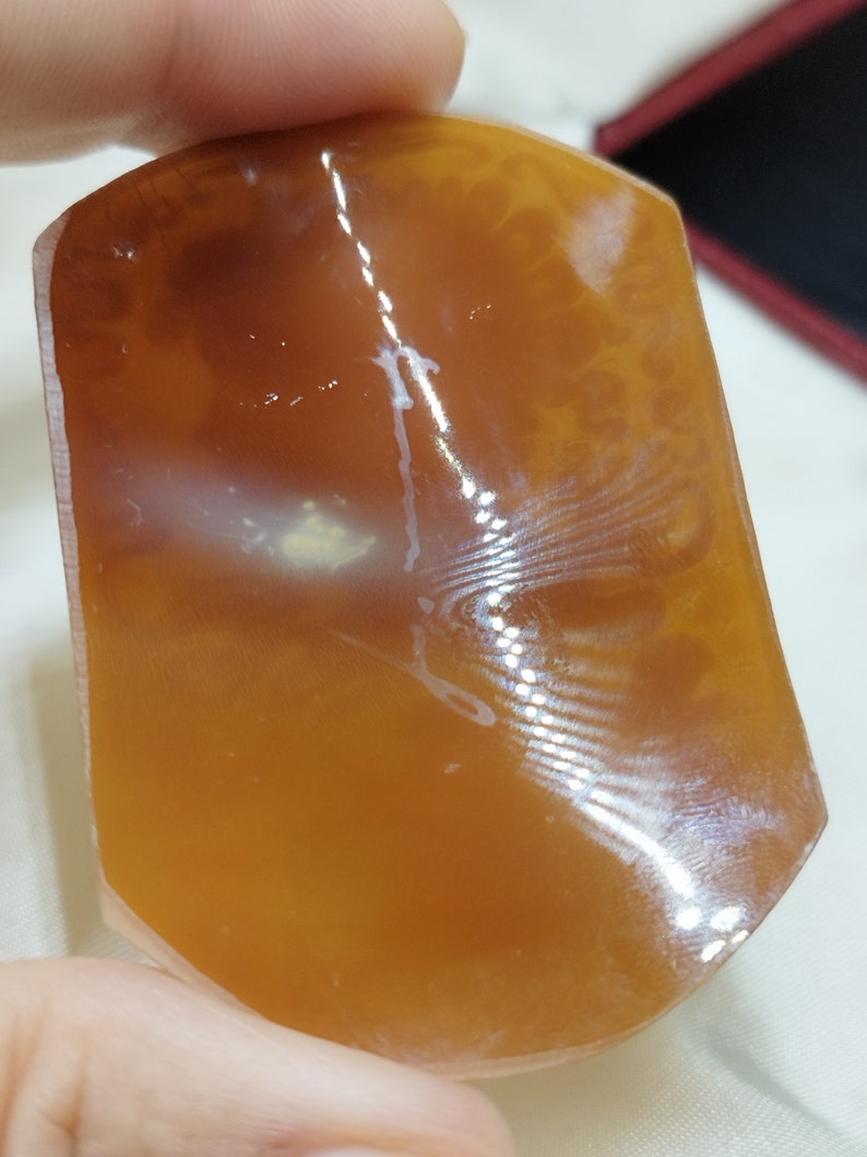 May include: A smooth, polished, orange agate stone with white veins and a translucent appearance.