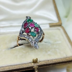 May include: A silver ring featuring a cluster of red and green gemstones set in a leaf-shaped design. The ring is displayed in a small, velvet-lined box.