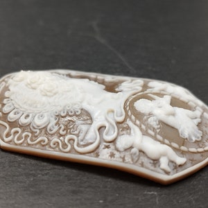 May include: A brown cameo pendant featuring a white carved design of a woman with a crown of flowers and two cherubs. The cameo is set in a silver tone frame.