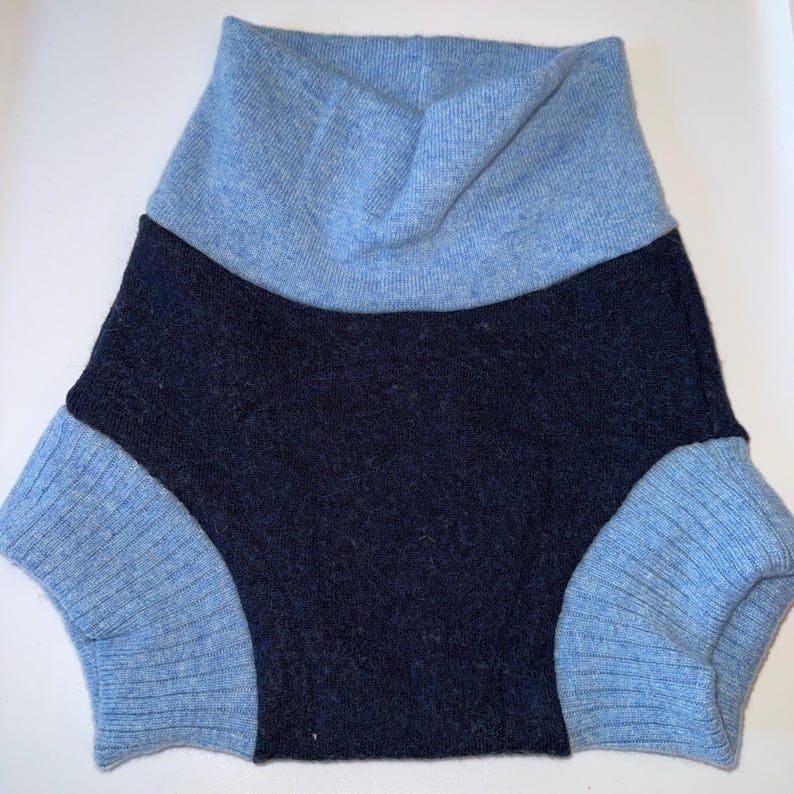 May include: A pair of knit shorts featuring a dark navy blue centre panel and a light blue waistband and leg cuffs. The garment is constructed from a soft, textured knit fabric with a ribbed pattern on the light blue sections and a solid knit.