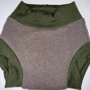 May include: A two-tone garment featuring an olive green high collar and side panels. The main body of the garment is a muted taupe colour. The fabric appears to be knitted.