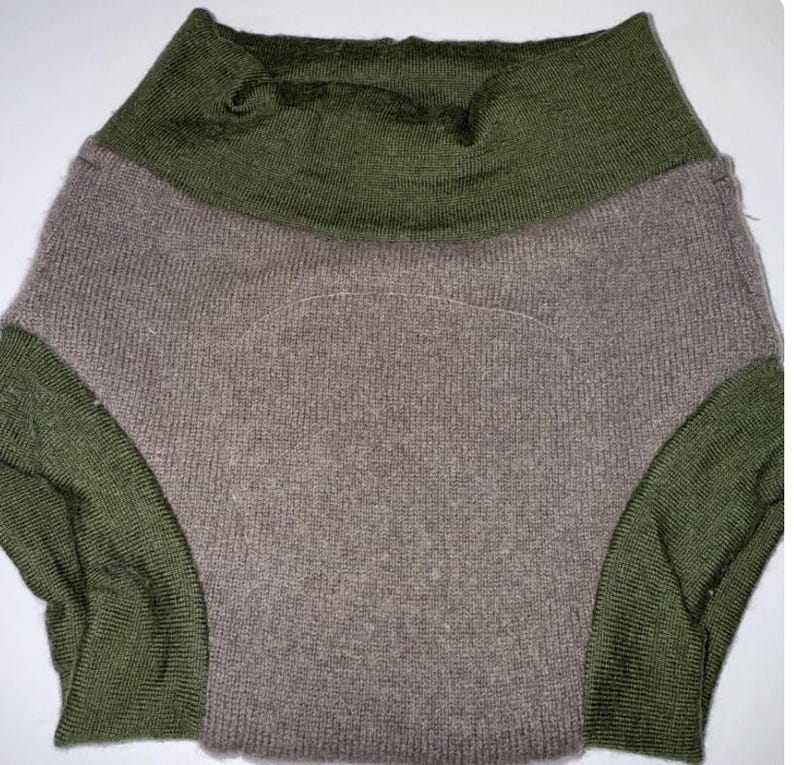 May include: A two-tone garment featuring an olive green high collar and side panels. The main body of the garment is a muted taupe colour. The fabric appears to be knitted.
