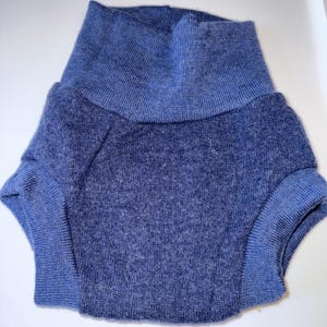 May include: A blue knit garment with a high, folded collar and short sleeves. The sleeves and collar are a lighter shade of blue than the body of the garment. The fabric appears soft and textured.