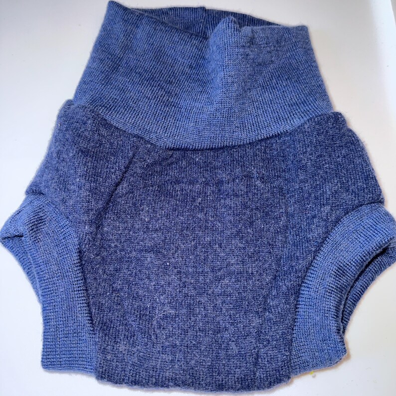 May include: A blue knit garment with a high, folded collar and short sleeves. The sleeves and collar are a lighter shade of blue than the body of the garment. The fabric appears soft and textured.