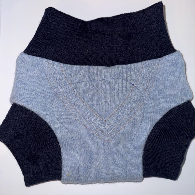May include: A light blue sweater with a V-neck design and navy blue accents. The sweater has navy blue sleeves and a navy blue collar. The sweater is folded, showing the front and part of the sleeves.