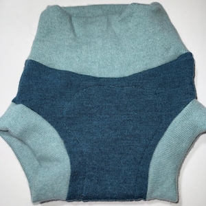 May include: A two-tone baby diaper cover in shades of teal and navy blue. The cover is made of a soft, knitted material. The waist and leg openings are teal, while the main body is navy blue.