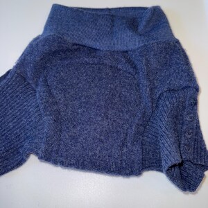 May include: A blue sweater with a wide, folded collar. The sweater has long sleeves and buttons on the cuff. The fabric appears to be a soft knit.