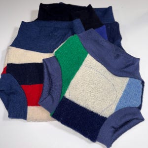 May include: A collection of colorful, patchwork-style knit garments. The garments feature a variety of colors, including navy, red, white, green, and blue. The knitwear has a ribbed collar and cuffs.