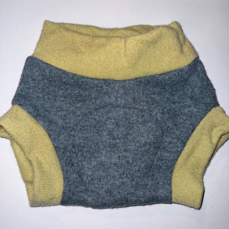 May include: A knitted garment, possibly for a pet, featuring a gray body and yellow trim around the waist and leg openings. The fabric appears soft and textured, with a folded-over waistband. The garment is designed to cover the midsection.