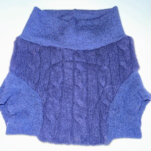 May include: A blue cable-knit sweater with a wide, ribbed collar. The sweater features a textured cable-knit design on the front and sleeves. The sleeves and collar are a lighter shade of blue.