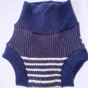 May include: A knitted garment featuring a high, solid navy blue waistband and a ribbed texture. The lower section displays a pattern of horizontal white and navy blue stripes, with solid navy blue ribbed leg openings for a secure fit.