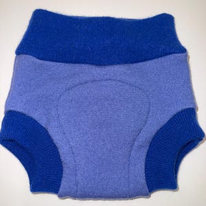 May include: A pair of blue and periwinkle-colored underwear. The underwear has a high waist and cuffs around the legs. The waist and leg cuffs are a darker shade of blue than the main body of the underwear.