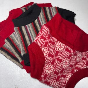 Puede incluir: Primer plano de prendas de punto dobladas. Una pieza es roja con un patrón geométrico blanco. Otra tiene rayas rojas y negras. La tercera es roja con cuello negro. Los artículos parecen ser suéteres o tops.