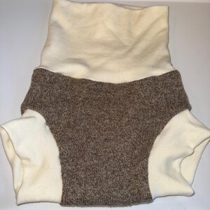 May include: A two-tone baby nappy cover. The top is a cream-coloured, ribbed fabric that folds over. The bottom is a brown, knitted fabric with cream-coloured leg openings. The nappy cover is designed to be soft and comfortable.
