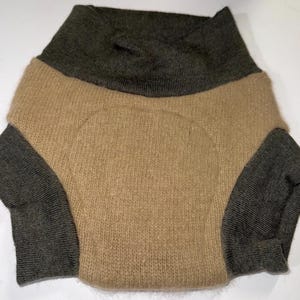 May include: A two-tone sweater in a neutral colour palette. The upper section and sleeves are a dark olive green, while the body is a light tan. The sweater has a high, folded collar and long sleeves. The knit fabric appears soft and warm.