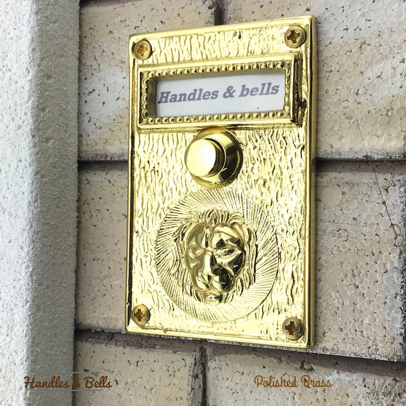 May include: A polished brass doorbell with a lion head design and a button. The doorbell has a label that says "Handles & bells".