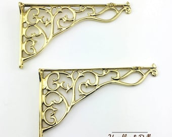 May include: Two gold metal shelf brackets with a decorative, ornate, scroll design. The brackets are in the shape of a right angle.