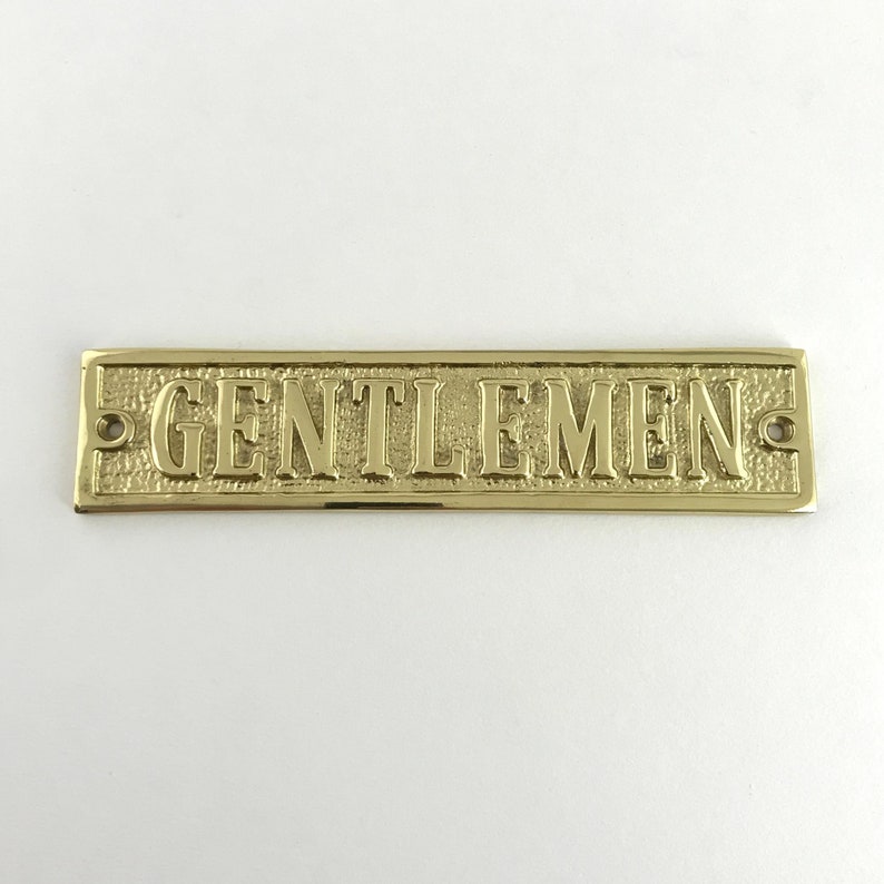 May include: A gold-colored brass sign with the word "GENTLEMEN" embossed on it.