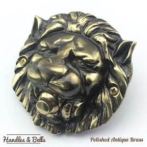 May include: A polished antique brass lion's head doorbell with a round button. The lion's head is detailed with a mane and a fierce expression. "Handles & Bells" and "Polished Antique Brass" are printed below the image.