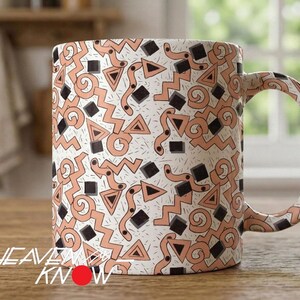 May include: A ceramic mug featuring a repeating pattern of peach-colored geometric shapes, including triangles, zigzags, and swirls, interspersed with small black squares and thin black lines on a white background, with a curved handle.