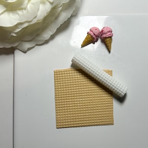 May include: Two pink ice cream cones with a waffle cone and a white waffle sheet.