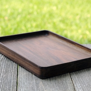 May include: A rectangular wooden serving tray with a dark brown finish. The tray is made of solid wood and has a smooth surface.