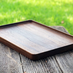 May include: A rectangular wooden serving tray with a dark brown finish. The tray has a smooth surface and rounded edges.