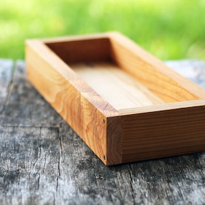 May include: A rectangular wooden tray with a natural wood finish. The tray has a smooth, polished surface and is made of solid wood.