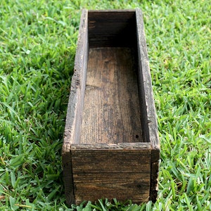 May include: A rustic wooden planter box with a dark brown stain. The planter is empty and ready to be filled with plants.