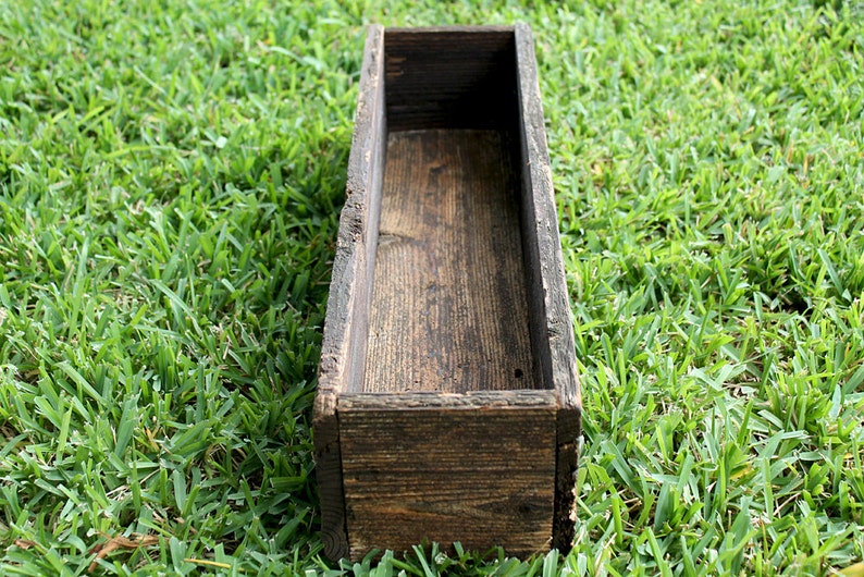 May include: A rustic wooden planter box with a dark brown stain. The planter is empty and ready to be filled with plants.