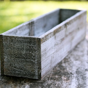 May include: A weathered white wooden planter box with a rectangular shape. The planter is made of reclaimed wood and has a rustic look.