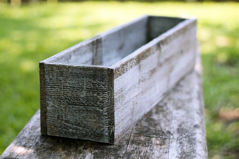 May include: A weathered white wooden planter box with a rectangular shape. The planter is made of reclaimed wood and has a rustic look.