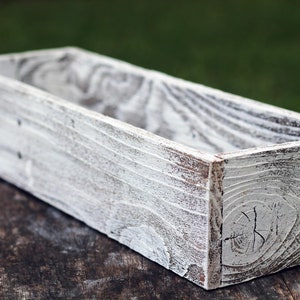 Puede incluir: Una jardinera de madera blanca con un acabado r&uacute;stico y desgastado. La jardinera es rectangular y tiene un dise&ntilde;o ancho y poco profundo.