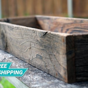 May include: A rustic wooden planter box with a weathered gray finish. The planter is made of reclaimed wood and has a rectangular shape.