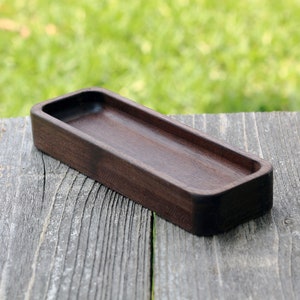 May include: A dark brown wooden tray with a rectangular shape and slightly rounded edges. The tray is made of solid wood and has a smooth, polished finish.