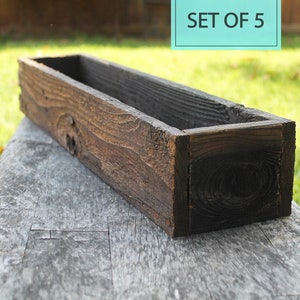 May include: Set of 5 rustic wooden planter boxes. The boxes are dark brown and have a weathered look. They are perfect for adding a touch of rustic charm to your home or garden.