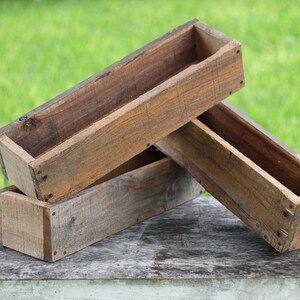 May include: Two wooden planter boxes stacked on top of each other. The boxes are made of rough-hewn wood and have a rustic appearance.