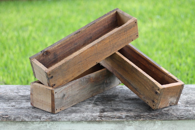 May include: Two wooden planter boxes stacked on top of each other. The boxes are made of rough-hewn wood and have a rustic appearance.
