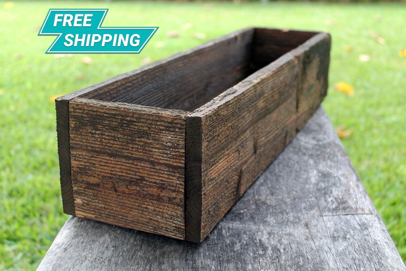 May include: A rustic wooden planter box with a dark brown stain. The planter is made of reclaimed wood and has a natural, weathered look.