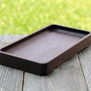 May include: A dark brown wooden tray with a rectangular shape. The tray is made of solid wood and has a smooth, polished finish.