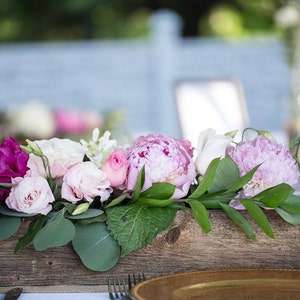 May include: A wooden box filled with pink, white, and purple flowers. The flowers are arranged in a rustic style and are surrounded by green leaves.