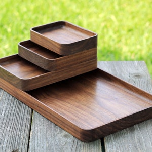 May include: Four wooden trays of varying sizes are stacked on top of each other. The trays are made of dark brown wood and have a smooth, polished finish.