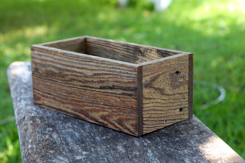 May include: A rustic wooden box with a natural wood finish. The box is empty and has a rectangular shape.