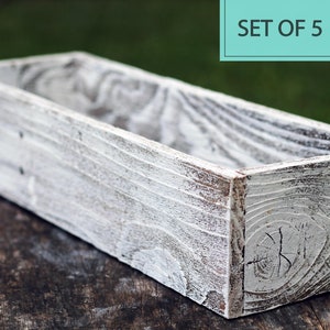 May include: Set of five whitewashed wooden rectangular planter boxes. The boxes are made of rustic wood and have a distressed white paint finish.  The boxes are perfect for displaying plants or flowers.
