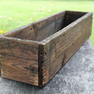May include: A rustic wooden planter box with a weathered brown finish. The box is empty and ready to be filled with plants.