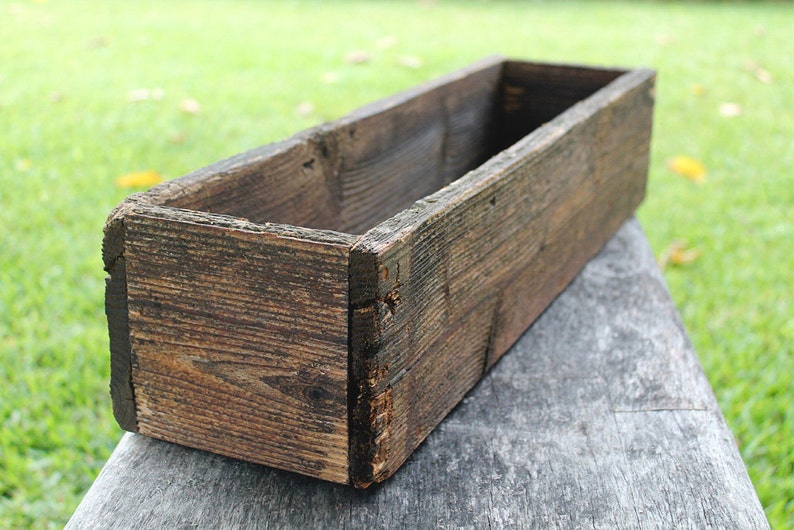 May include: A rustic wooden planter box with a weathered brown finish. The box is empty and ready to be filled with plants.