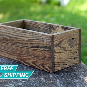 May include: A rectangular wooden planter box with a rustic brown finish. The planter is made of reclaimed wood and has a natural wood grain pattern.