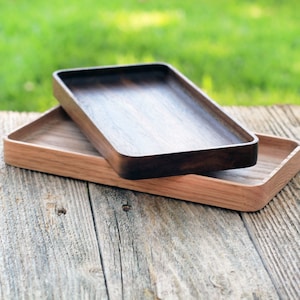 May include: Two wooden trays, one dark brown and one light brown, are stacked on top of each other on a weathered wooden surface.