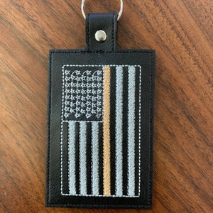 May include: Black leather keychain with a thin gold line down the centre of an embroidered American flag.