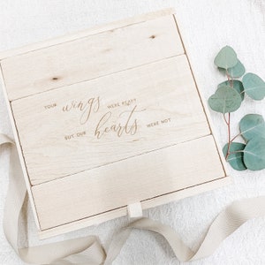 May include: A wooden box with a hinged lid and a fabric tie closure. The box is engraved with the text "Your wings were ready but our hearts were not".